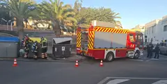 Los bomberos apagando el fuego en uno de los contenedores en presencia de agentes de la Polic&iacute;a Nacional