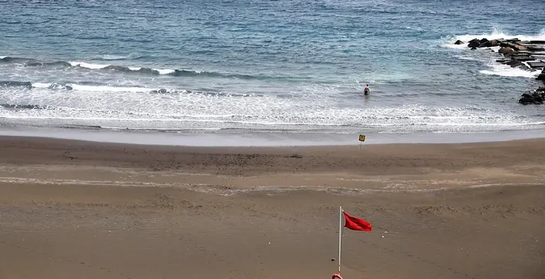 Un bañista entrando al mar con bandera roja.