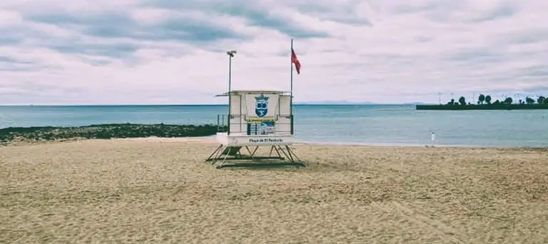 Izada la bandera roja en la Playa de El Reducto, Al fondo a la derecha la Punta del Camello donde el Consorcio del Agua y Canal Gestión tienen en aliviadero del emisario, originario de la contaminación 