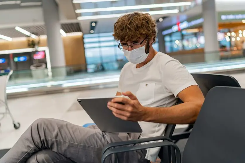 Man in respirator mask is waiting next plane at the airport and using  tablet. Coronavirus COVID-19 concept.