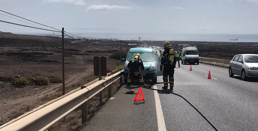 Imagen de los bomberos apagando el fuego situado en el motor del coche.