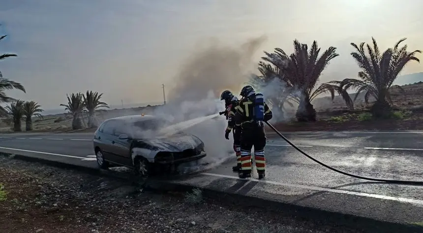 Los bomberos sofocando el incendio del vehículo en la carretera
