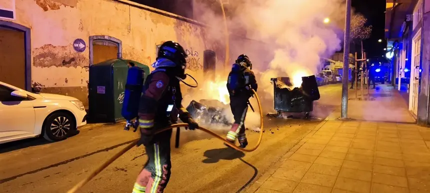 Bomberos apagando el fuego de un contenedor que se encontraba en medio de la carretera.