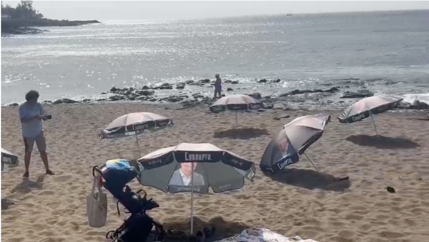 Imagen de playa Bastián llena de sombrillas con la cara de Pedro Sánchez.