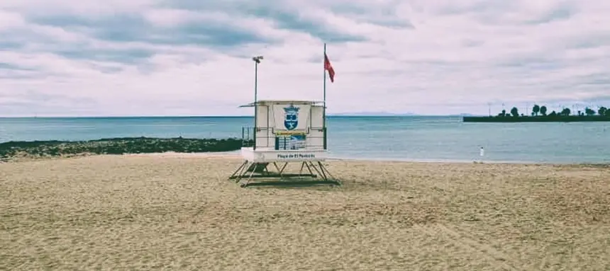 Izada la bandera roja en la Playa de El Reducto, Al fondo a la derecha la Punta del Camello donde el Consorcio del Agua y Canal Gestión tienen en aliviadero del emisario, originario de la contaminación 