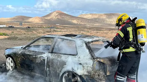 Operario de los bomberos apagando el fuego dentro del vehículo en la entrada a Costa Teguise..