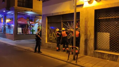 Bomberos del Consorcio durante la reparación del cristal del escaparate dañado.