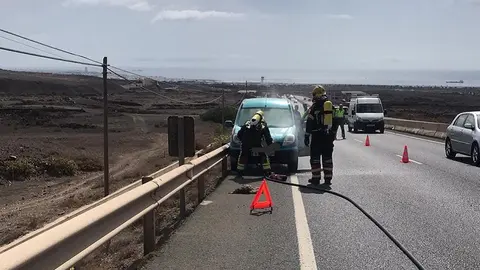 Imagen de los bomberos apagando el fuego situado en el motor del coche.
