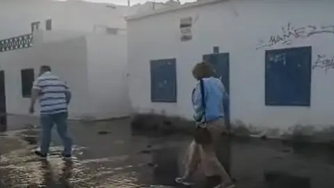 Imagen de unos turistas esta semana pasando por encima de la tubería rota en el Charco. 