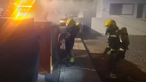 Momento de la actuación de los bomberos para sofocar el fuego del contenedor