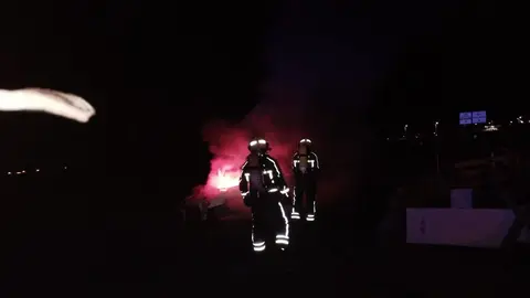 Actuación de los bomberos con el coche incendiado.