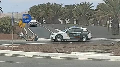 Ciclista afectado en el suelo junto a la Guardia Civil.