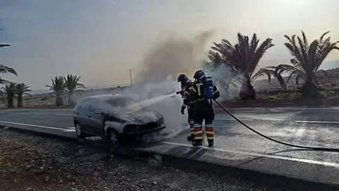 Los bomberos sofocando el incendio del vehículo en la carretera