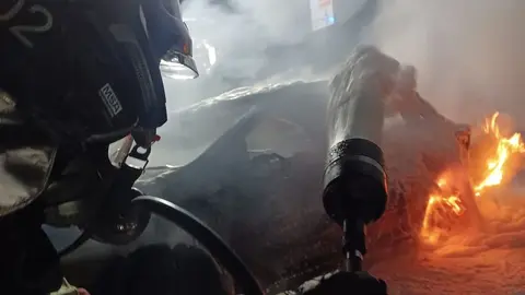 Instante en el que uno de los bomberos lanza la espuma contra el fuego del vehículo