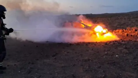 Un bombero extingue el fuego del coche en llamas.