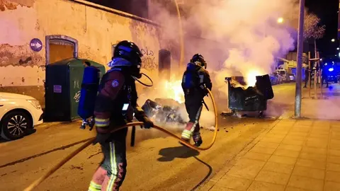Bomberos apagando el fuego de un contenedor que se encontraba en medio de la carretera.