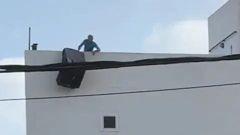 Imagen de un individuo lanzando un sofá desde una azotea.