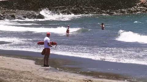 Un socorrista observa a dos bañistas en el agua, en una playa con oleaje y fuertes corrientes.