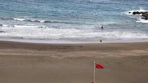 Un bañista entrando al mar con bandera roja.