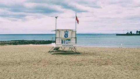 Izada la bandera roja en la Playa de El Reducto, Al fondo a la derecha la Punta del Camello donde el Consorcio del Agua y Canal Gestión tienen en aliviadero del emisario, originario de la contaminación 