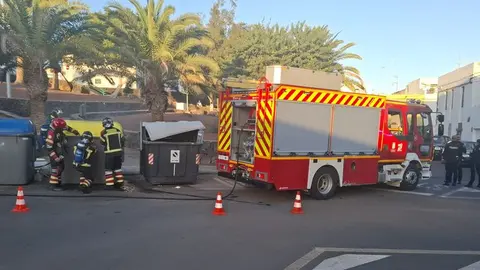 Los bomberos apagando el fuego en uno de los contenedores en presencia de agentes de la Polic&iacute;a Nacional