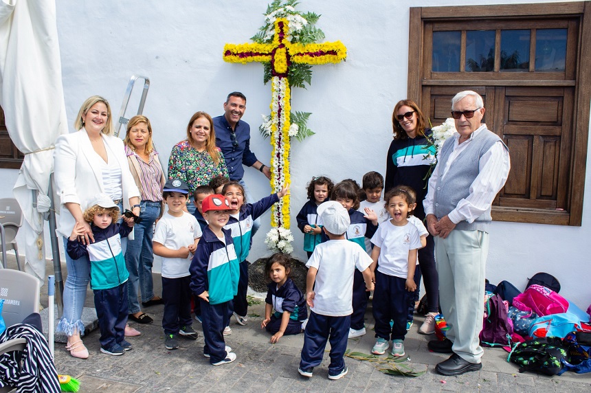 Oswaldo Betancort y Nori Machín junto a una cruz llena de flores y varios niños del colegio de Teguise.