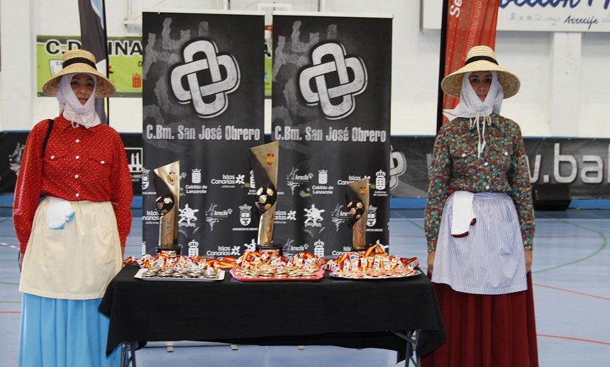 Imagen de dos mujeres vestidas con el traje tradicional junto a las medallas y trofeos que fueron entregadas a los tres primeros clasificados.